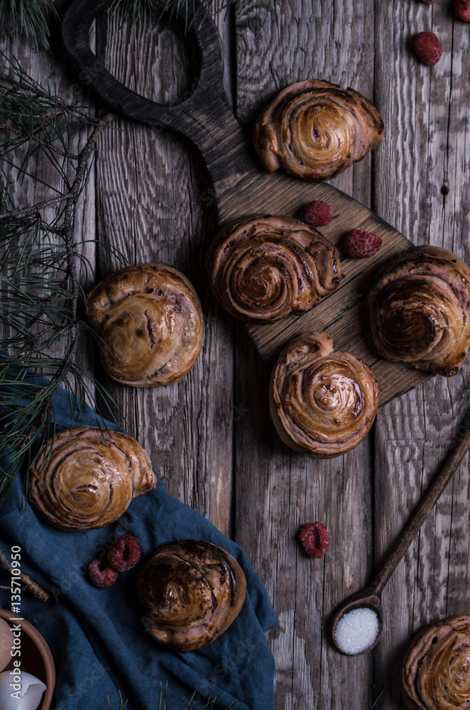 Buns with white chocolate and raspberries on a wooden table with pieces of chocolate, berries and pine branches