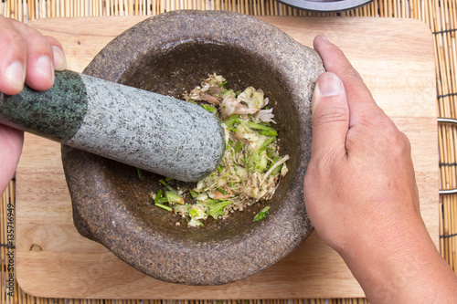 Chef pound coriander, pepper and garlic with pestle on mortar