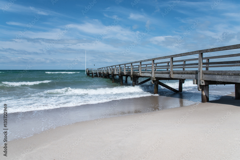 pier with stormy sea under blue sky with scattered clouds