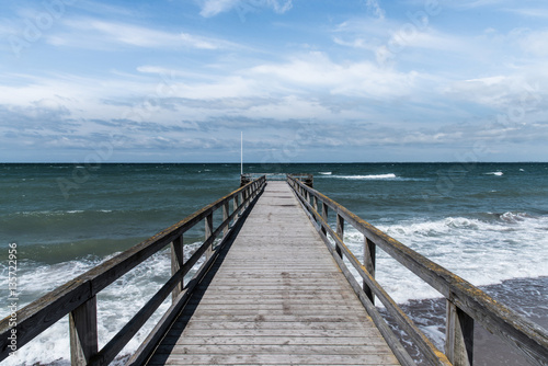 pier with stormy sea under blue sky with scattered clouds