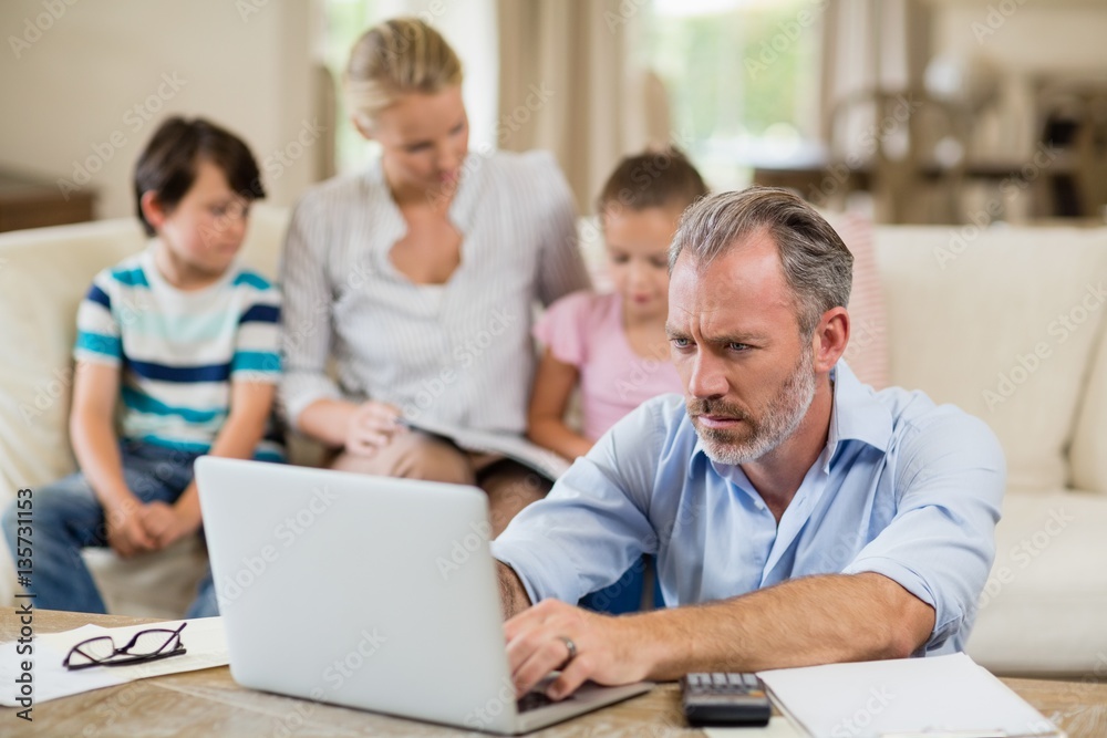 Man using laptop with bills on table in living room