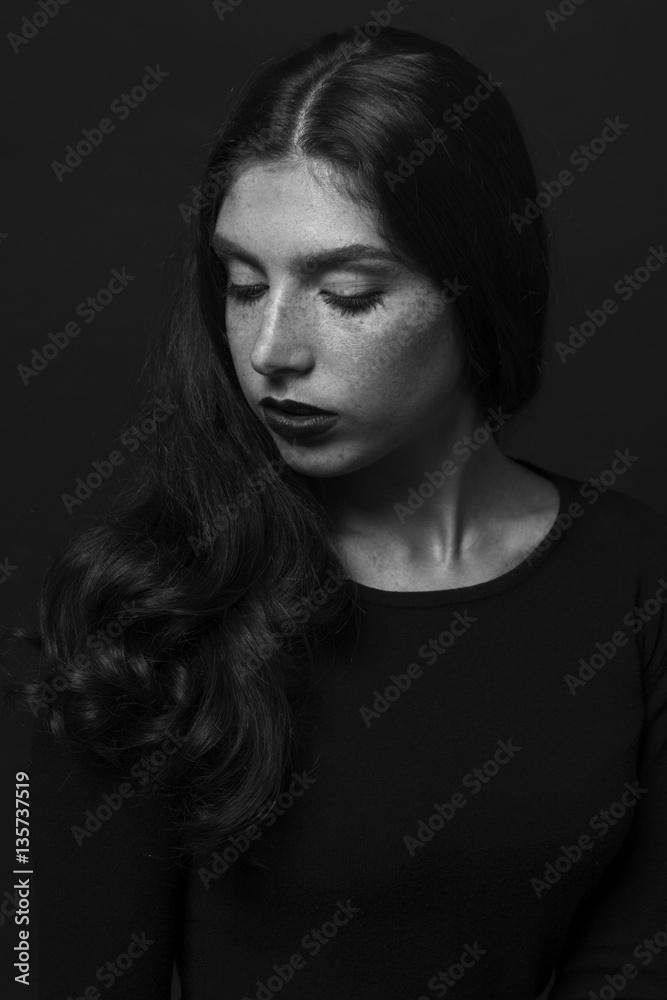 Black and white portrait of a sad girl dressed in black blouse. Devush with long curly hair. Gentle make-up and beautiful freckles.
