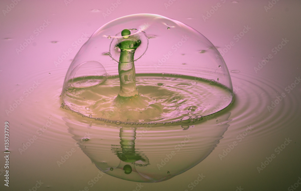 Seifenblase mit eintretendem grünen Wassertropfen auf rosa Hintergrund