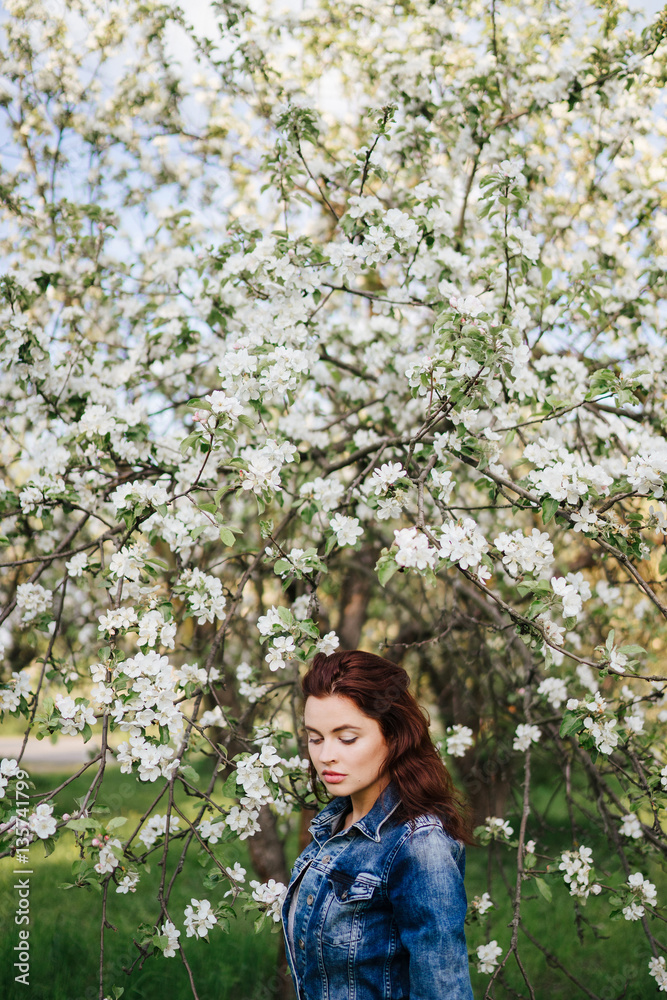Young pretty sexy caucasian woman in jeans jacket standing near blooming spring tree. Youth, freshness, beauty, happiness concept. Healhty hair, clean skin. Young pretty sexy caucasian woman in jeans jacket standing near blooming spring tree. Youth, freshness, beauty, happiness concept. Healhty hair, clean skin.