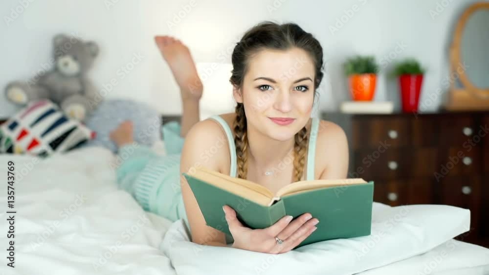 Pretty girl in pyjamas reading book and smiling to the camera
Pretty girl in pyjamas reading book and smiling to the camera