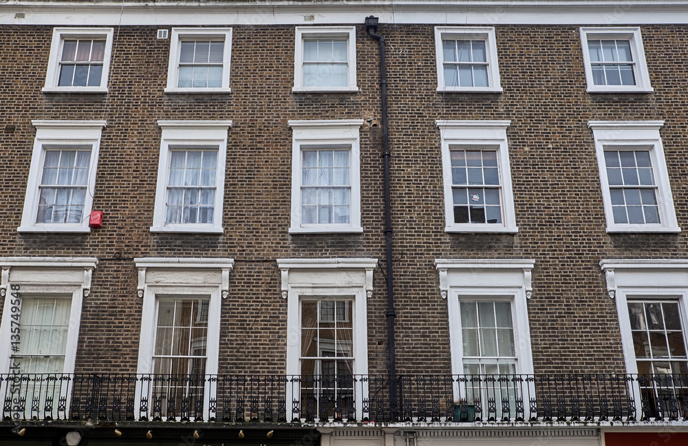 Brown brick facade with white decorations around rectangle shaped colonial style windows of a british apartment building in London City