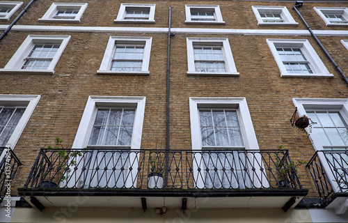 Brown brick facade with white decorations around rectangle shaped colonial style windows and balconies of a british apartment building in London City