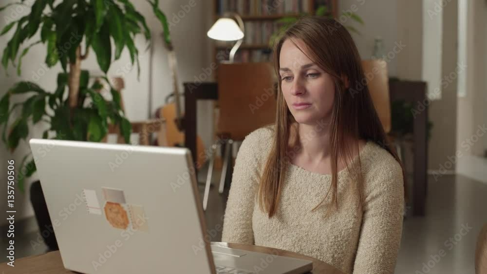 Young woman watches videos on internet in her laptop at home. She watches very concentrated and serious with a suddenly look of disgust. Dolly shot to the left. Young woman watches videos on internet in her laptop at home. She watches very concentrated and serious with a suddenly look of disgust. Dolly shot to the left.