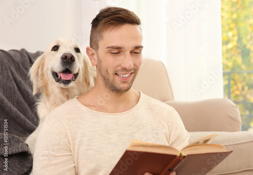 Young man reading book with dog at home