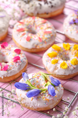Delicious donuts and flowers on baking rack and wooden table, closeup