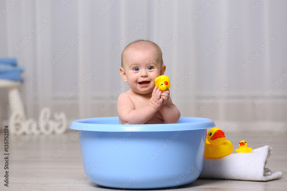 Cute baby playing with rubber duck while sitting in plastic basin at home Cute baby playing with rubber duck while sitting in plastic basin at home