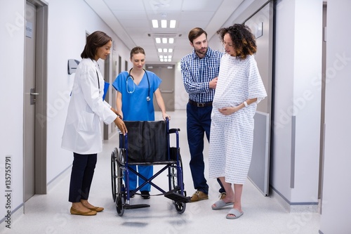 Man and doctors assisting pregnant woman to sit on wheelchair