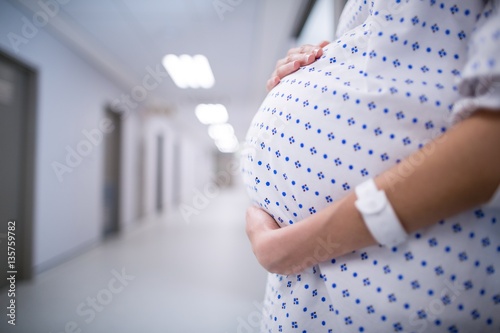 Fototapeta Mid section of pregnant woman standing in corridor