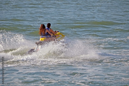 Two young women riding tandem on a high speed jet ski.
