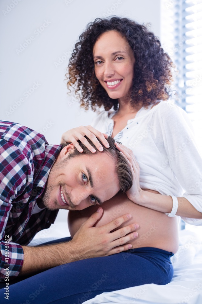 Fototapeta premium Smiling man listening to pregnant womans belly in ward