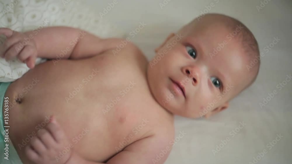 Happy newborn baby yawns closeup in white bed