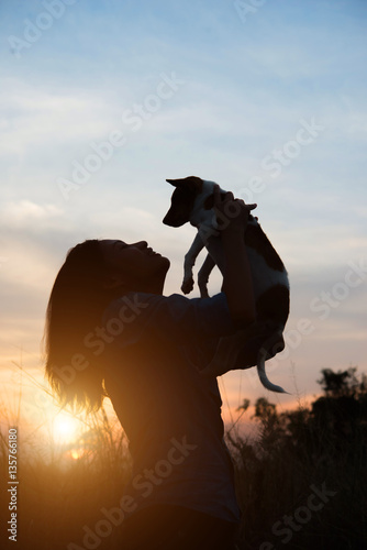 silhouette of woman holding small dog at sunset field. © Johnstocker