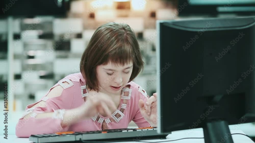 Girl with Down syndrome sitting at a computer at home and typing text.