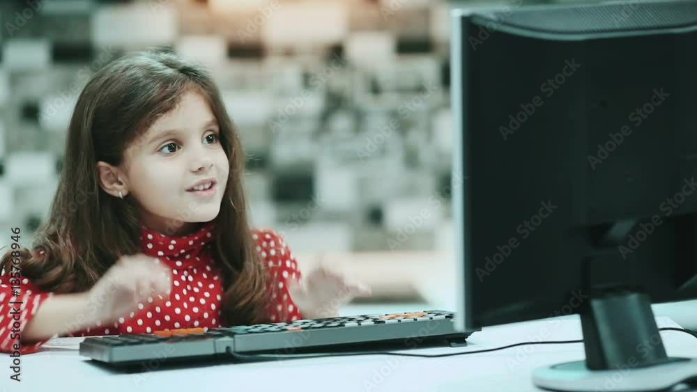 Little schoolgirl with dark hair and a blouse with polka dots, work at home computer, typing text.