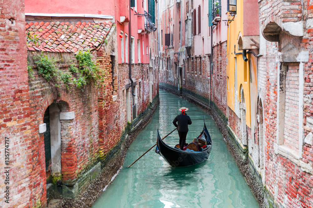 Naklejka premium Venetian gondolier punting gondola przez zielone wody kanału w Wenecji Włochy