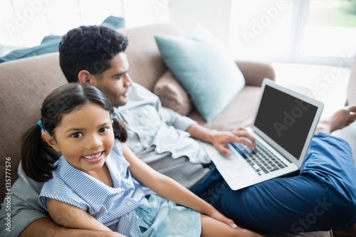 Father and daughter sitting on sofa and using laptop
