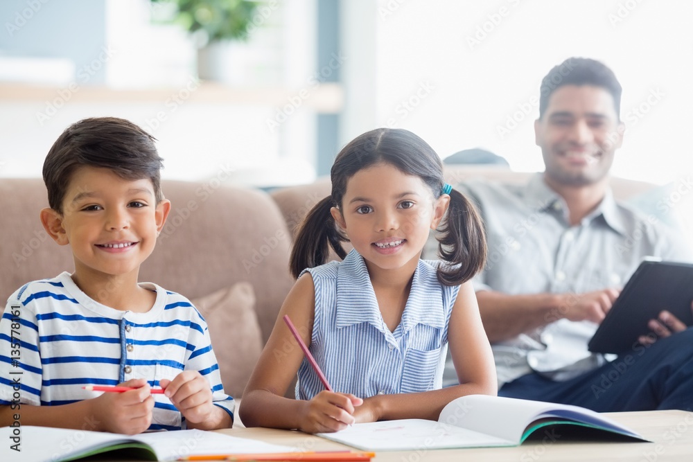 Smiling siblings doing homework in living room at home Smiling siblings doing homework in living room at home