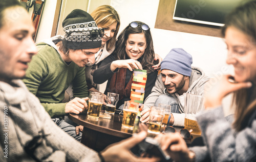 Happy friends playing table board game while drinking beer at pub - Cheerful people having fun at brewery bar corner - Friendship concept on contrast desaturated filter with soft greenery color tones