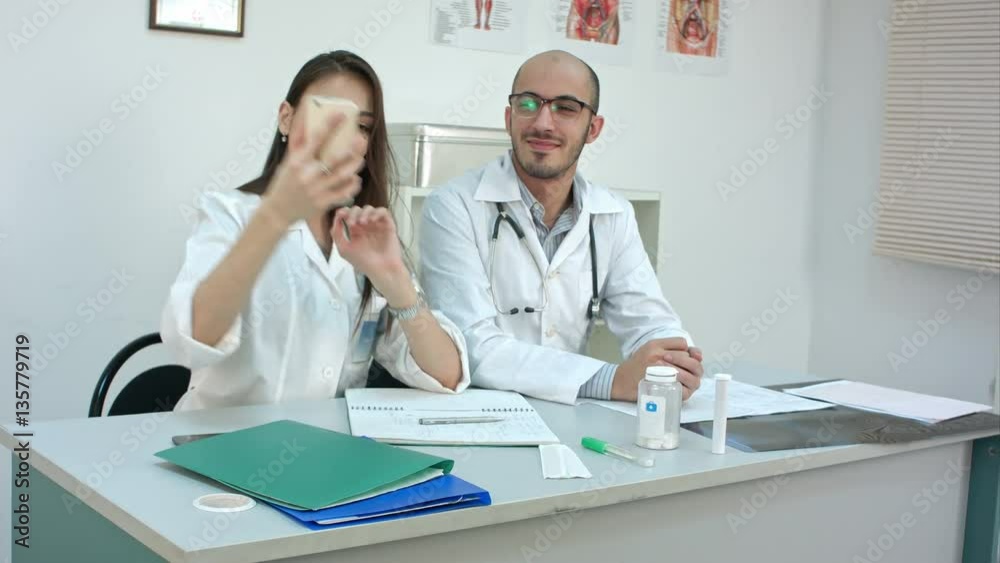 Young doctor and pretty nurse taking selfies on the phone at their desk Young doctor and pretty nurse taking selfies on the phone at their desk