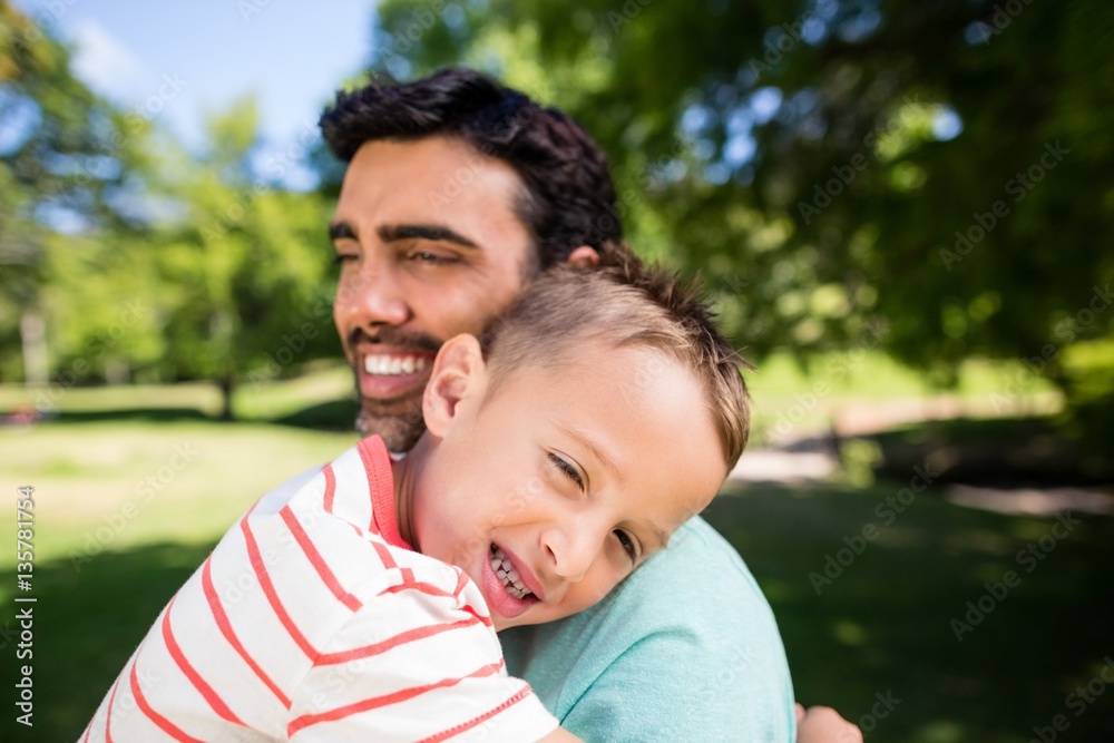 Son smiling while embracing his father in park Son smiling while embracing his father in park