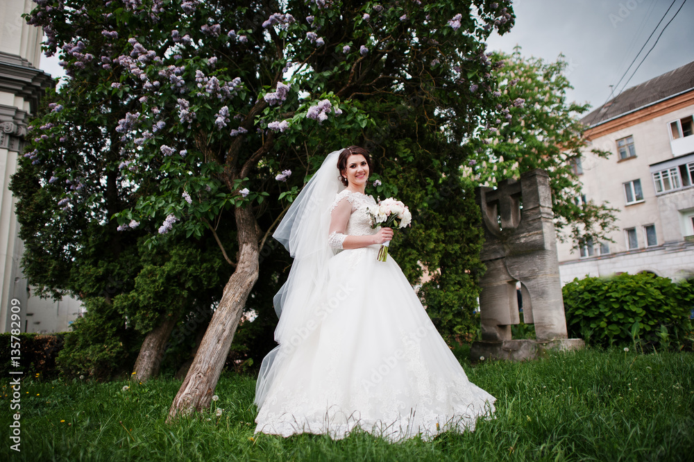 Cute brunette bride under lilac tree with wedding bouquet at han