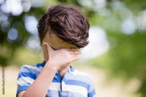 Boy covering eyes with hand in park