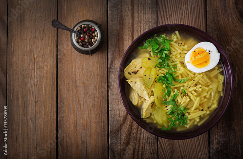 Noodle soup with chicken, celery and egg in a bowl on a old wooden background. Flat lay. Top view.