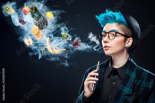 hipster woman with blue hair smoking fruit electronic cigarette on black background. Vape advertisement concept. Copy space photo