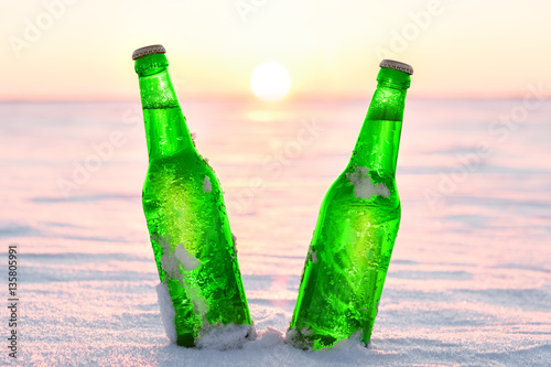 Two bottles of cold beer on the snow at sunset. Close up view.