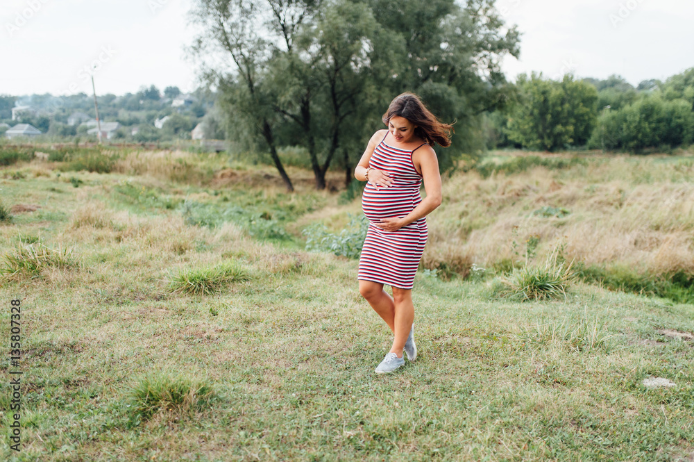 Pregnant woman in strip dress walking in park Pregnant woman in strip dress walking in park