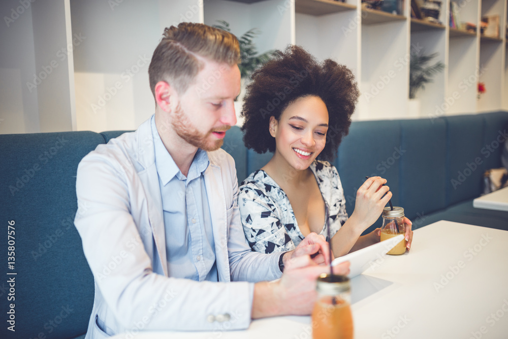 Obraz premium Happy middle age interracial couple sitting in cafe bar, smiling and looking at white tablet.