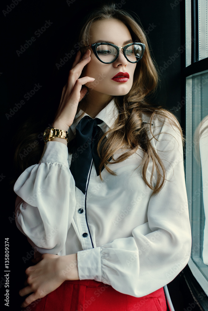 Indoor portrait of a young beautiful fashionable business woman posing in  loft interior. Model looking through window. Lady wearing stylish clothes. Female  fashion concept. Dark background. Waist up Photos