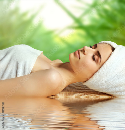 Young woman relaxing in spa salon and reflection on water surface