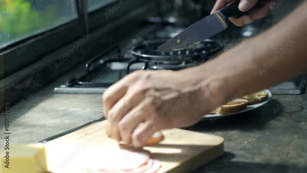 Man cutting ham and preparing sandwich in kitchen, focus on hands
Man cutting ham and preparing sandwich in kitchen, focus on hands