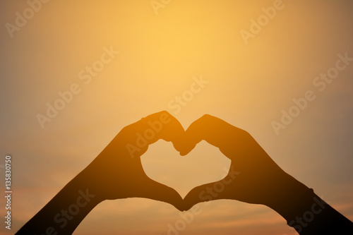 Silhouette of hand in the heart shape at the sky sunset backgroud