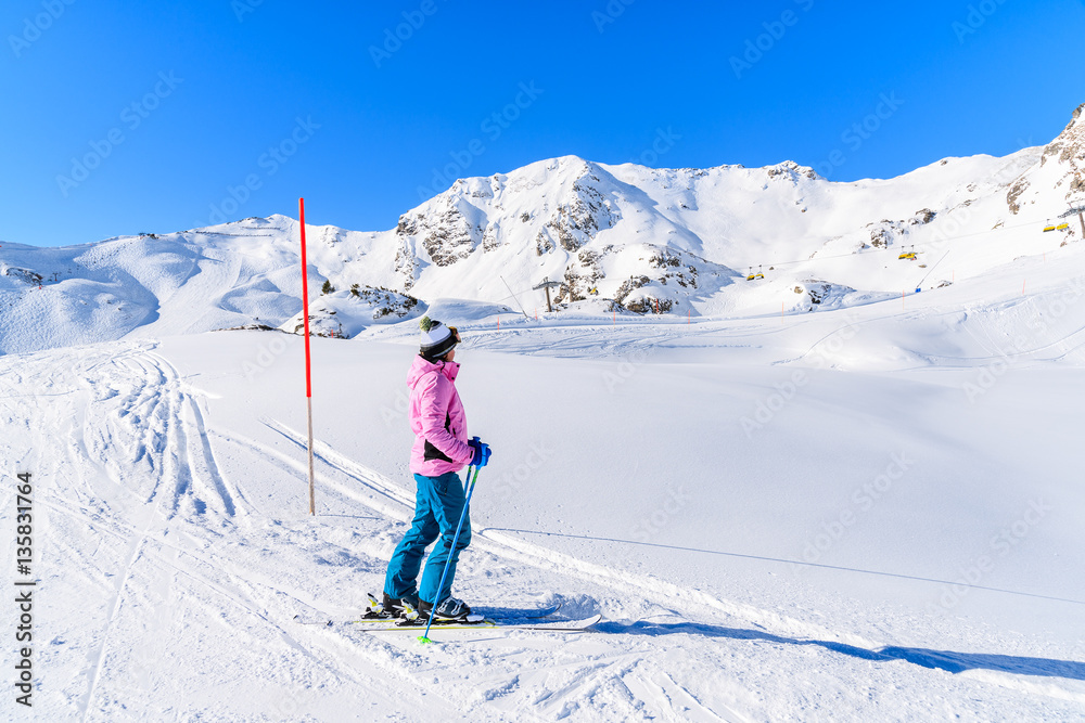 Young woman skier standing on ski slope and looking at mountains in Obertauern ski area, Austria