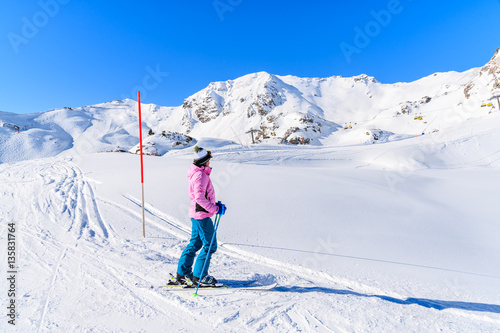 Young woman skier standing on ski slope and looking at mountains in Obertauern ski area, Austria