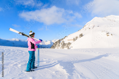 Young woman skier holding skis and looking at mountains in Obertauern ski area, Austria
