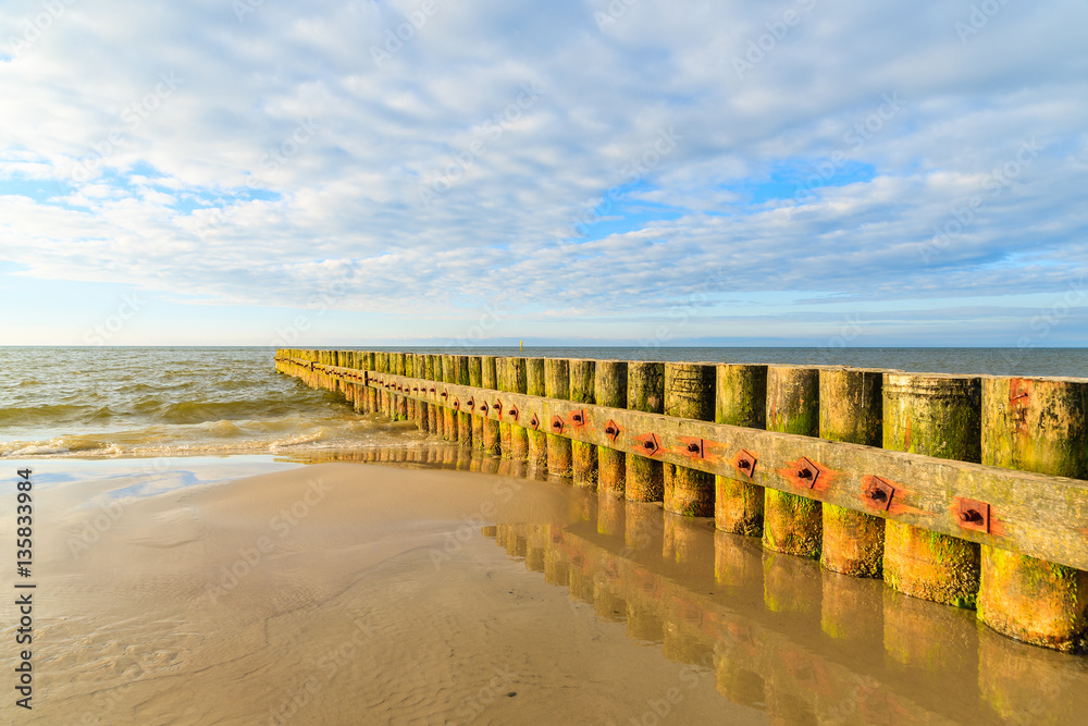 Wooden breakwaters on Leba beach during sunny day with clouds, Baltic Sea, Poland