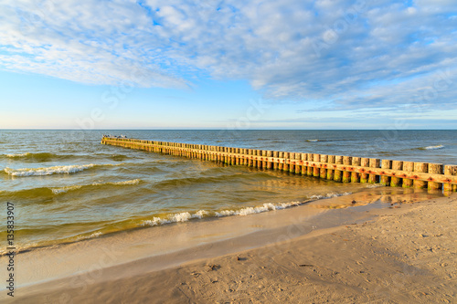 Wooden breakwaters on Leba beach during sunny day with clouds  Baltic Sea  Poland