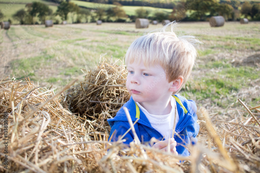 Young blond boy playing in hayfield Young blond boy playing in hayfield