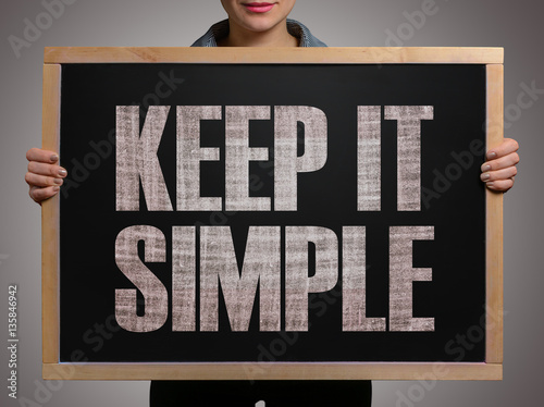 Girl (manager, student, businesswoman) in casual clothes holding a black chalk board with the text Keep it simple photo