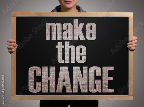 Girl (manager, student, businesswoman) in casual clothes holding a black chalk board with the text Make the change