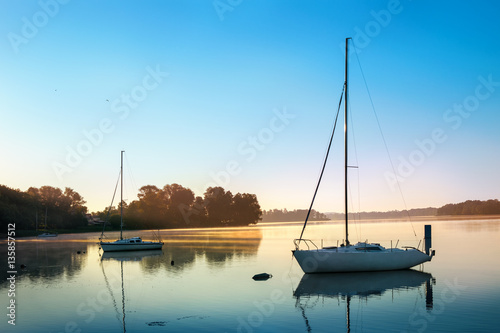 Fototapeta Naklejka Na Ścianę i Meble -  Yachts float on the calm waters of the lake. Early morning. Masuria, Poland .