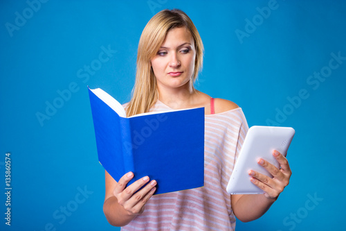 Blonde woman choosing between book and tablet